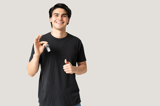 Portrait of good looking young man in casual showing car key against gray background