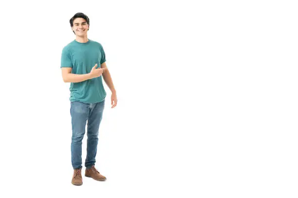 Good looking Hispanic young man pointing towards copy space in studio with white background