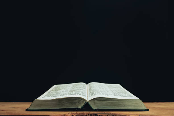 istock Open Holy Bible on a red old wooden table. Beautiful Black wall background. 1258126495