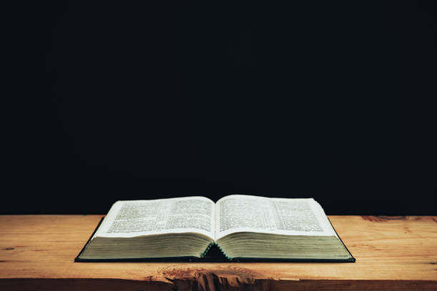 istock Open Holy Bible on a red old wooden table. Beautiful Black wall background. 1258126522
