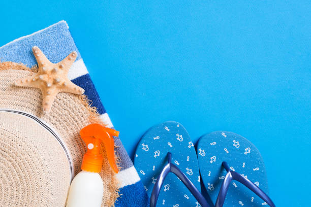 istock Summer beach flat lay accessories. Sunscreen bottle cream, straw hat, flip flops, towel and seashells on colored Background. Travel holiday concept with copy space 1258131098