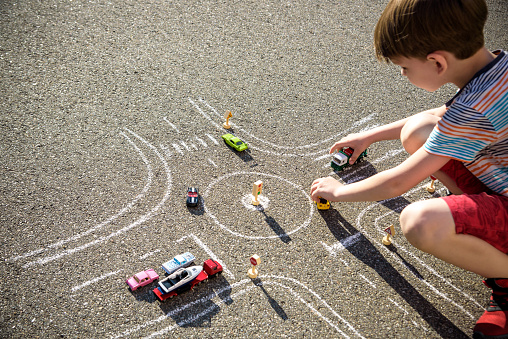 Funny kid boy having fun with picture drawing traffic car with chalks. Creative leisure for children outdoors in summer. Difficult traffic rules concept.
