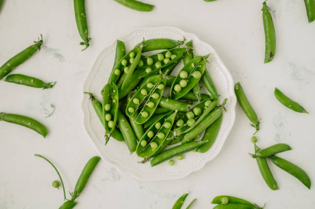 istock Green fresh peas in a white plate on a white table. 1258134473