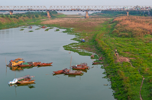 Long Bien bridge at sunset by the red river with fishing boats, Hanoi, North Vietnam.