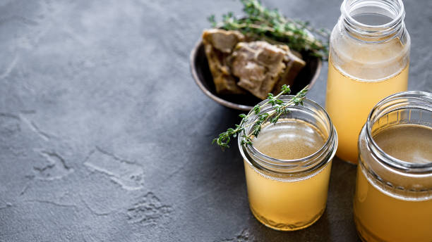 glass jar with yellow fresh bone broth on dark gray background - caldo imagens e fotografias de stock