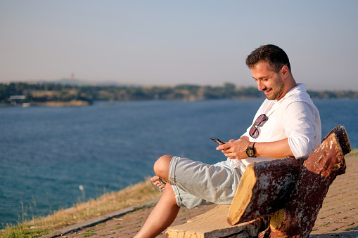a man sitting on bench alone, looking at his mobile phone
