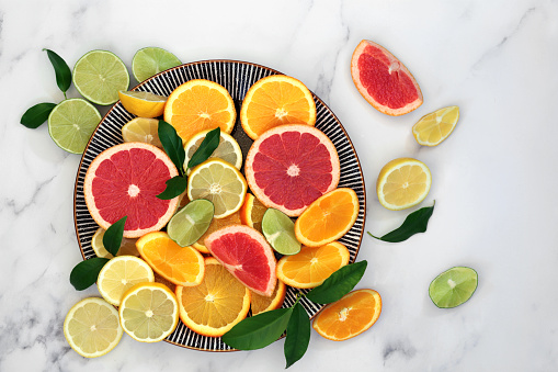 Immune boosting citrus fruit health food with orange, lemon, grapefruit &   leaves on round plate and marble background. Super foods high in antioxidants, vitamins, dietary fibre & anthocaynins. Top view.