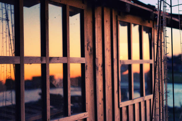 Gujean-Mestras, France - July 11, 2020. View of part of a wooden oyster hut in the Arcachon basin. In the foreground, the sunset is reflected in the windows of the cabin. In the background, part of the banks of the basin and the colorful sky are visible.