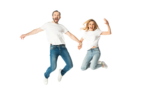 happy adult couple in white t-shirts holding hands while jumping isolated on white