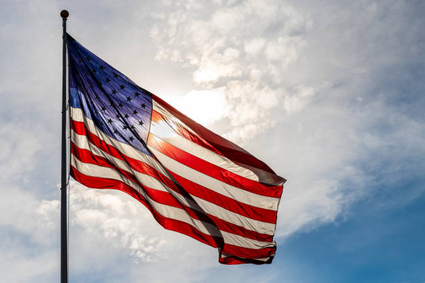 istock Large American flag glowing from backlight from the sun, against cloudy sky 1258164715