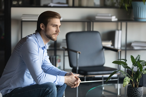 Pensive young Caucasian man sit on chair look in distance thinking or pondering over problem solution, thoughtful male employee lost in thoughts, make plan or decision, have dilemma at workplace