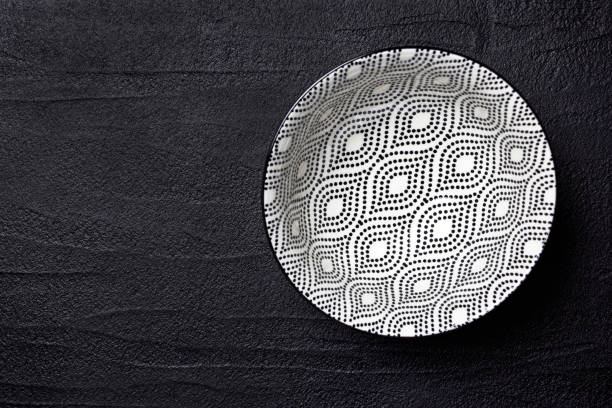 Empty black and white bowl on a black concrete background, top view with empty space.