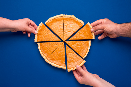 Top view with a home-baked pumpkin pie isolated on a blue colored background. Three people grabbing with their hand's slices of pumpkin cake