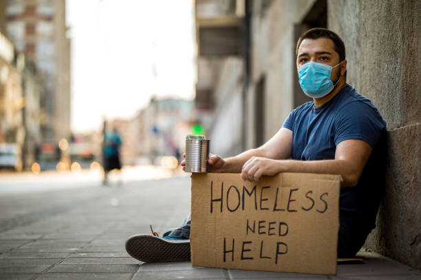 istock Homeless man sitting and asking for help while holding cardboard 1258172745