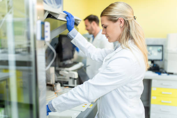 Female Scientist Working in The Laboratory With Colleague. Female doctor using a machine to conduct a medical test. Doctor working with centrifuge pharmaceutical machine and putting samples into it. drug manufacturing stock pictures, royalty-free photos & images