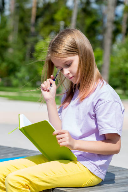 istock school girl sitting on bench in public park and making notes to her note book 1258202587