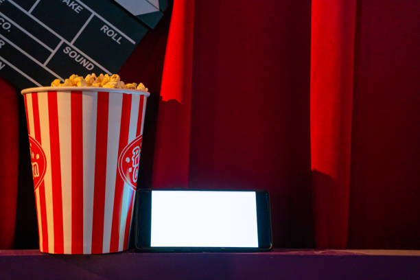 istock mobile phone with empty white bright screen with popcorn bucket and movie clapper board. Concept of streaming TV on internet phone. 1258260813