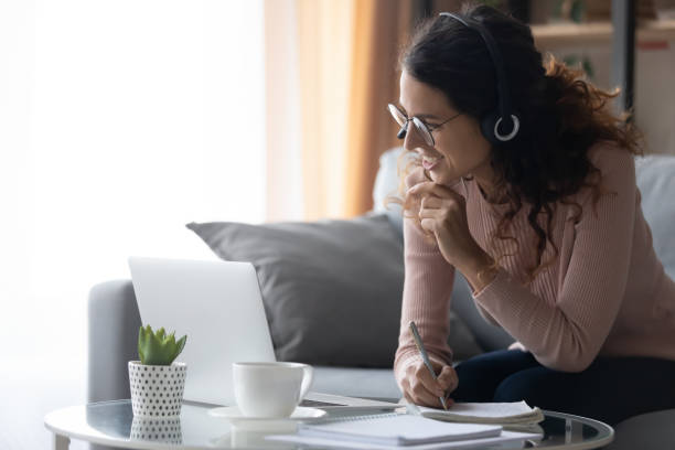 istock Smiling young woman in headset make notes studying on laptop 1258280052