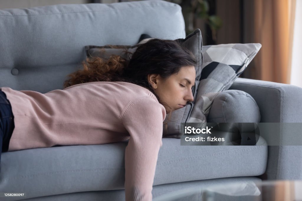 Tired young woman sleeping on couch at home Exhausted young Caucasian woman lying on comfortable sofa in living room sleeping after hard-working day, tired millennial female fall asleep on couch at home, take nap or daydream, fatigue concept Tired Stock Photo