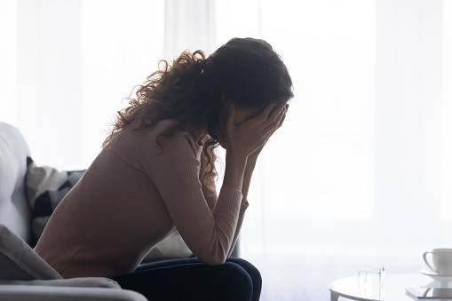 Sad young woman sit on sofa crying suffering from relationships problems, unhappy Caucasian female feel lonely abandoned, stressed about mental or psychological trouble, cheating, divorce concept