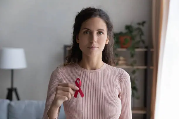 Headshot portrait of young Caucasian woman hold red ribbon breast cancer symbol support sick people patients, profile picture of millennial female raise HIV AIDS disease awareness, healthcare concept