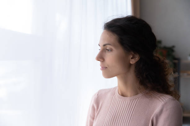 istock Pensive young woman look in window thinking or missing 1258280111