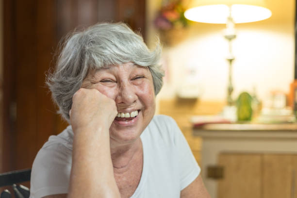 Senior lady laughing out loud at home Senior lady chatting on the living room, laughing with stories at home, after dinner. relieved face stock pictures, royalty-free photos & images
