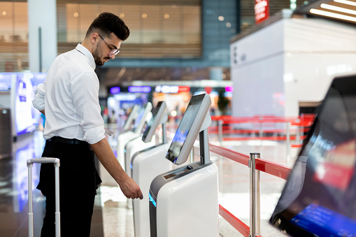 Young Passenger at the self-service check-in machine in departure hall at airport.