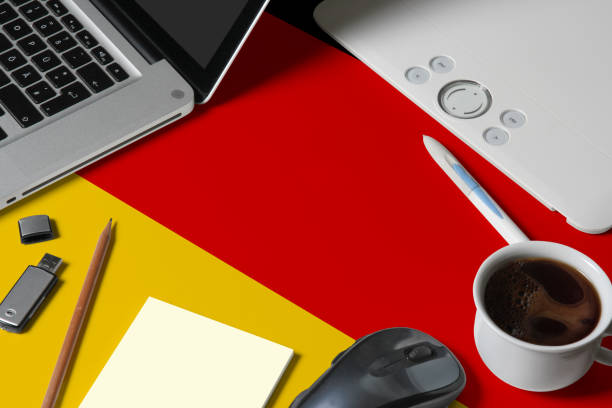 Germany national flag on top view work space of creative designer with laptop, computer keyboard, usb drive, graphic tablet, coffee cup, mouse on wooden table.