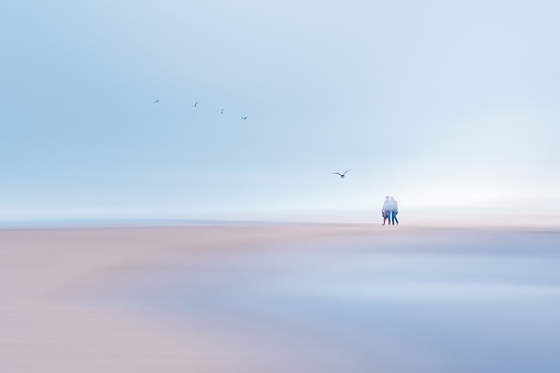 Abstract seascape. Sky, beach, ocean, and silhouette of walking people. Soft light, motion blur, long exposure