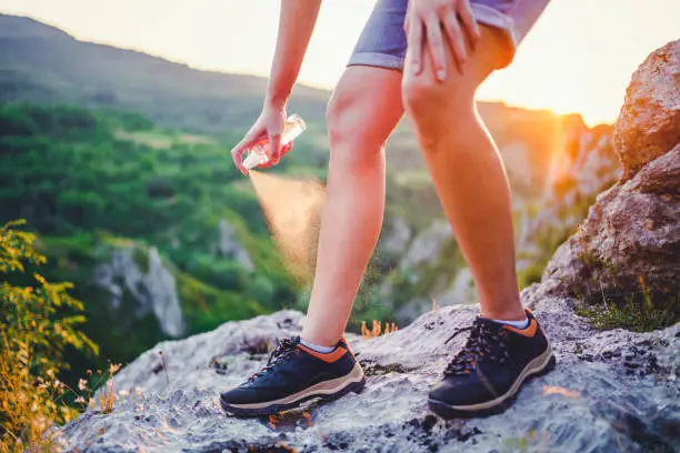 Hiker woman applying anti mosquito repellent on the leg during hiking in nature