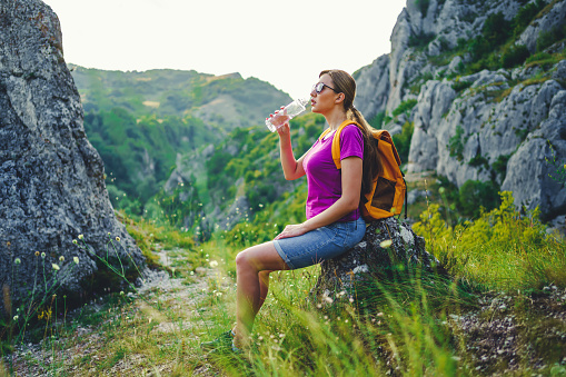 Young tourist woman hiker with backpack resting in nature and drinking water