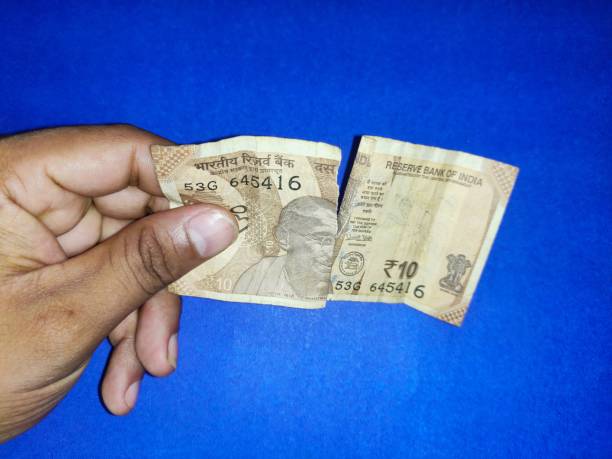 istock Torn Ten rupees Indian note in hand on blue background 1258304937