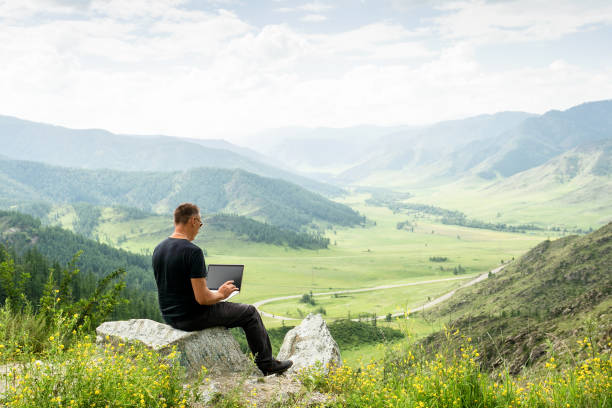 istock Traveler blogger work remote on netbook computer while enjoying mountain nature landscape view outdoors. man working outdoors with laptop. 1258351690