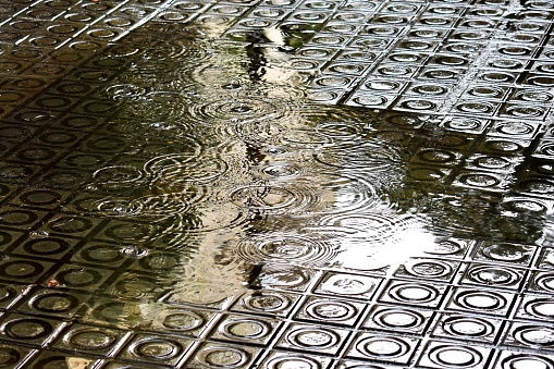 Rain drops falling into a puddle on the sidewalk of Barcelona, Spain.