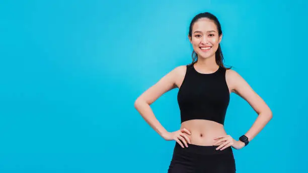 Photo of Portrait of confident beautiful asian fitness woman standing after exercise isolated on blue colour background with copy space.Concept of slim and healthy happy girl workout.