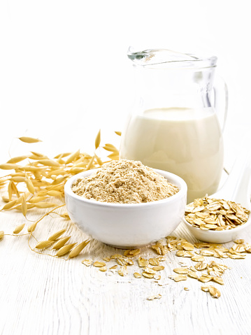 Flour oat in bowl, milk in a jug, oatmeal in spoon, oaten stalks on the background of wooden table