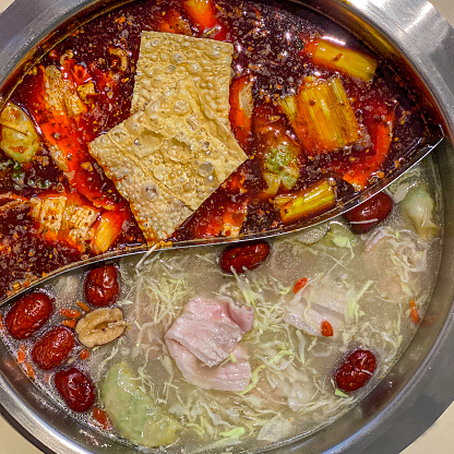 A pot of half hot peppercorn (ma la) and clear soup steamboat serves with bean curb, meat ingredient in a metal pot. It beings togetherness and family bonding eating together