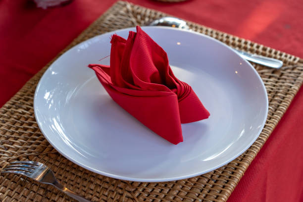 istock Elegant table setting with fork, spoon, white plate and red napkin in restaurant . Nice dining table set with arranged silverware and napkins 1258522581