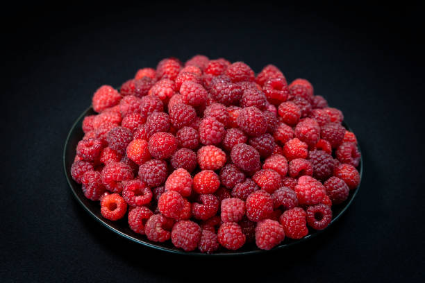 istock Fresh organic raspberries in a plate on black background 1258522685