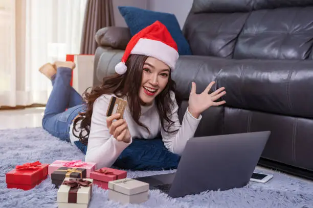 cheerful woman in santa hat shopping online for Christmas gift with laptop in the living room