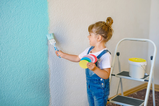 Young Mexican woman creating outdoor mural on the roof top wall. She is dressed in casual outfit. Exterior of old building in the city of Toronto, Canada..