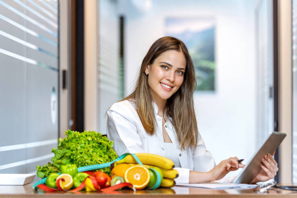Dietician working on diet plan with digital tablet Smiling nutritionist in her office, she is showing healthy vegetables and fruits. tablet pc and digital hospital tools stock pictures, royalty-free photos & images