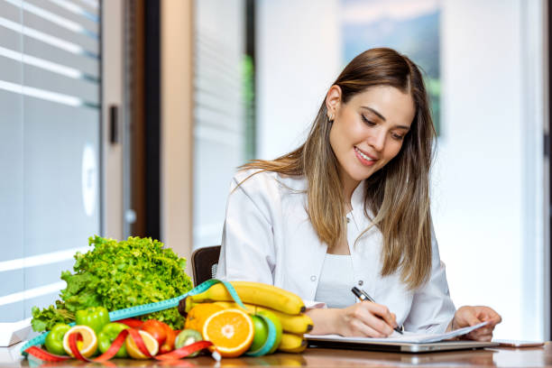 Dietician working on diet plan with digital tablet Smiling nutritionist in her office, she is showing healthy vegetables and fruits. nutritionist stock pictures, royalty-free photos & images