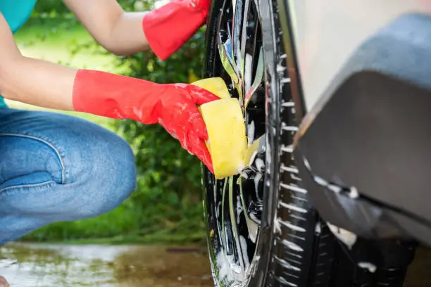woman holding sponge washing the wheels of her car