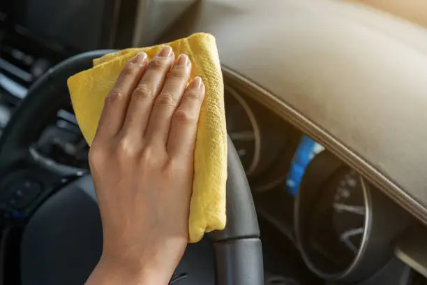 hand cleaning steering wheel of car with yellow microfiber cloth