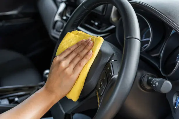 hand cleaning steering wheel of car with yellow microfiber cloth