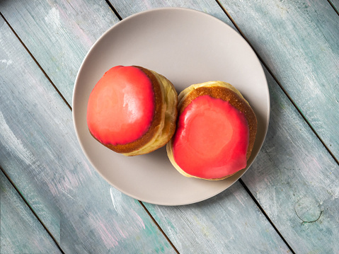 Donuts with strawberry icing on a light plate on a wooden background top view