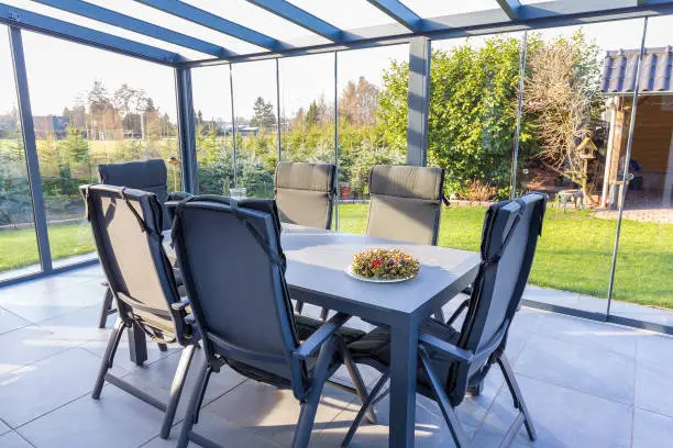 Conservatory of glass with table and chairs in garden. In this room you can enjoy sunny days even when the temperature outdoors is too low. It's as if you are outdoors in your garden.