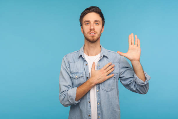 i swear! portrait of honest responsible man in worker denim shirt giving evidence with raised hand, blue background - proof of love imagens e fotografias de stock